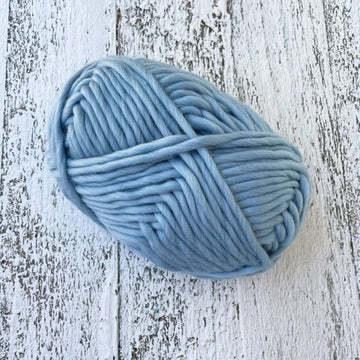 A ball of light blue super chunky merino yarn in a colourway called Dream, sitting on a textured wooden background.