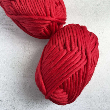 Two balls of super chunky merino yarn in a scarlet red colour on a grey backdrop.